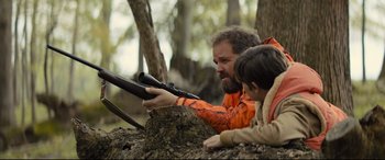Movie still from “Brightburn” (2019), directed by David Yarovesky – A man and a boy holding a rifle in the woods; Medium shot, Over the shoulder angle