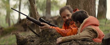 Movie still from “Brightburn” (2019), directed by David Yarovesky – A man and a boy with a rifle in the woods; Medium shot, Over the shoulder angle