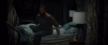 Movie still from “Brightburn” (2019), directed by David Yarovesky – A man sitting on top of a bed in the dark; Medium shot, High angle