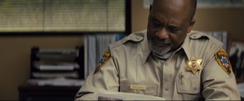 Movie still from “Brightburn” (2019), directed by David Yarovesky – A man wearing a uniform looking down at a book; Close Up shot, High angle