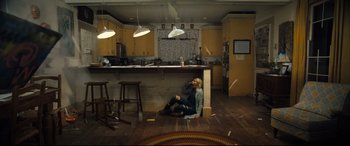 Movie still from “Brightburn” (2019), directed by David Yarovesky – A woman sitting on the floor of a kitchen next to a counter; Wide shot, High angle