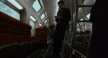 Movie still from “Source Code” (2011), directed by Duncan Jones – A man standing on a train looking at his cell phone; Wide shot, Low angle