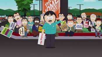 Movie still from “South Park: Joining the Panderverse” (2023), directed by Trey Parker – A man holding a sign standing in front of a group of people; Medium shot, High angle