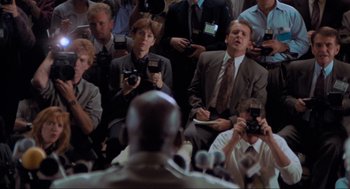 Movie still from “Space Jam” (1996), directed by Joe Pytka – A group of people sitting in a room with microphones; Medium shot, Over the shoulder angle