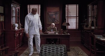 Movie still from “Space Jam” (1996), directed by Joe Pytka – A man sitting at a desk in front of another man standing in front of a desk; Wide shot, Low angle