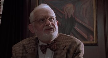 Movie still from “Space Jam” (1996), directed by Joe Pytka – An older man wearing a suit and bow tie in front of a painting; Close Up shot, Over the shoulder angle
