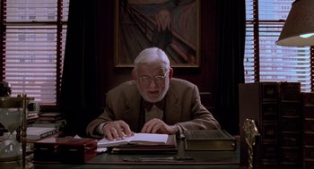 Movie still from “Space Jam” (1996), directed by Joe Pytka – An older man sitting at a desk looking at a book; Medium shot, Low angle