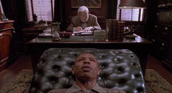 Movie still from “Space Jam” (1996), directed by Joe Pytka – A man sitting in a chair in front of an old man; Medium shot, Low angle