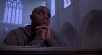 Movie still from “Space Jam” (1996), directed by Joe Pytka – A man sitting at a table with his hands clasped together; Close Up shot, Low angle