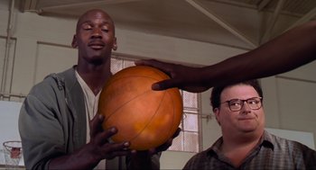 Movie still from “Space Jam” (1996), directed by Joe Pytka – A man holding an orange basketball in front of another man; Medium shot, Over the shoulder angle