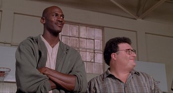 Movie still from “Space Jam” (1996), directed by Joe Pytka – A man and a man standing next to each other in front of a window; Medium shot, Low angle