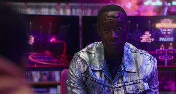 Movie still from “Space Jam: A New Legacy” (2021), directed by Malcolm D. Lee – A man in a silver jacket sitting in front of a purple background; Medium shot, Over the shoulder angle