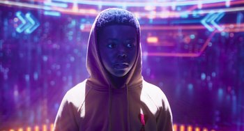 Movie still from “Space Jam: A New Legacy” (2021), directed by Malcolm D. Lee – A young man wearing a hooded sweatshirt in front of a purple background; Medium shot, Low angle