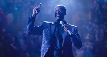 Movie still from “Space Jam: A New Legacy” (2021), directed by Malcolm D. Lee – A man holding a microphone while standing in front of an audience; Medium shot, Low angle