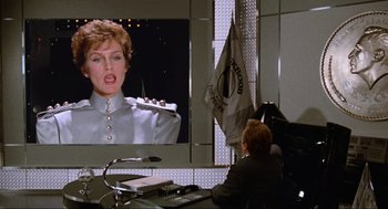 Movie still from “Spaceballs” (1987), directed by Mel Brooks – A man sitting at a desk in front of a large screen tv; Medium shot, Over the shoulder angle