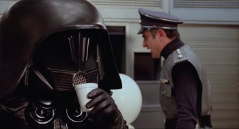 Movie still from “Spaceballs” (1987), directed by Mel Brooks – A man in a helmet holding a coffee cup; Close Up shot, Over the shoulder angle