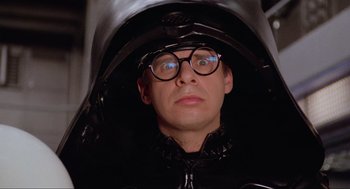 Movie still from “Spaceballs” (1987), directed by Mel Brooks – A man in a black outfit and glasses; Close Up shot, Over the shoulder angle
