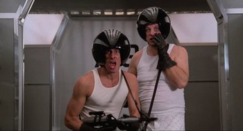 Movie still from “Spaceballs” (1987), directed by Mel Brooks – Two men in white tank tops and black helmets are posing for a picture; Medium shot, Low angle