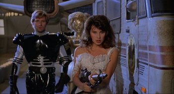 Movie still from “Spaceballs” (1987), directed by Mel Brooks – A woman in a white dress holding a gun in front of a robot; Medium shot, Over the shoulder angle