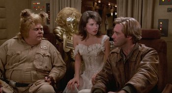 Movie still from “Spaceballs” (1987), directed by Mel Brooks – A woman in a white dress sitting next to two men; Medium shot, Over the shoulder angle