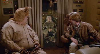 Movie still from “Spaceballs” (1987), directed by Mel Brooks – Two people are sitting in a room with a painting of a monk; Wide shot, Over the shoulder angle