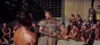 Movie still from “Spartacus” (1960), directed by Stanley Kubrick – A group of men sitting on the beach and a man in a roman outfit; Medium shot, Over the shoulder angle