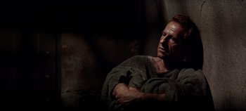 Movie still from “Spartacus” (1960), directed by Stanley Kubrick – A man wrapped in a towel is sitting in a dark room; Medium shot, Low angle