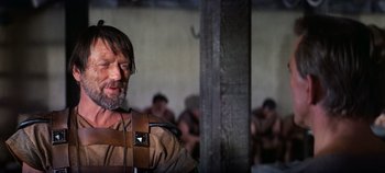 Movie still from “Spartacus” (1960), directed by Stanley Kubrick – A man with a beard and a leather harness on; Close Up shot, Over the shoulder angle