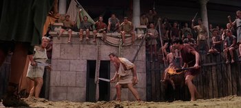 Movie still from “Spartacus” (1960), directed by Stanley Kubrick – A man holding a baseball bat while standing in front of a group of people; Wide shot, High angle