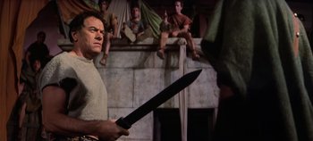 Movie still from “Spartacus” (1960), directed by Stanley Kubrick – A man holding a large black sword in front of a group of people; Medium shot, Low angle