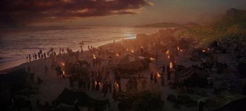 A crowd of people gathered on the beach at sunset