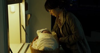Movie still from “Broker” (2022), directed by Kore-eda Hirokazu – A woman is holding a baby in a basket; Medium shot, High angle