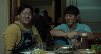 Movie still from “Broker” (2022), directed by Kore-eda Hirokazu – Two people sitting at a table in front of a plate of food; Medium shot, Low angle