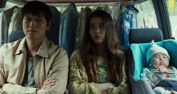 Movie still from “Broker” (2022), directed by Kore-eda Hirokazu – A young woman standing next to a man in front of clothes; Medium shot, Over the shoulder angle