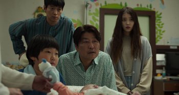 Movie still from “Broker” (2022), directed by Kore-eda Hirokazu – A group of people standing next to each other in a room; Medium shot, Over the shoulder angle