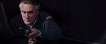 Movie still from “Speed” (1994), directed by Jan de Bont – An older man in a military jacket holding a gun; Close Up shot, Overhead angle