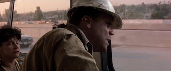 Movie still from “Speed” (1994), directed by Jan de Bont – A man wearing a hard hat looking out of a window; Close Up shot, Over the shoulder angle