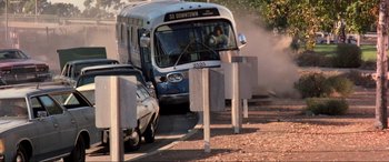 Movie still from “Speed” (1994), directed by Jan de Bont – A city bus driving down a street next to parked cars; Wide shot, Over the shoulder angle