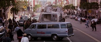 Movie still from “Speed” (1994), directed by Jan de Bont – A silver van driving down a street next to buildings; Wide shot, Low angle