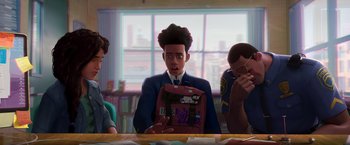 Movie still from “Spider-Man: Across the Spider-Verse” (2023), directed by Joaquim Dos Santos – A man is sitting at a table in front of other people; Medium shot, Over the shoulder angle