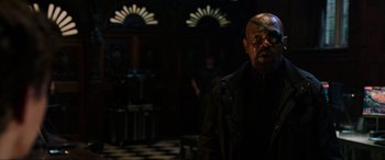 Movie still from “Spider-Man: Far from Home” (2019), directed by Jon Watts – A man in a black jacket is standing in a dark room; Medium shot, Over the shoulder angle