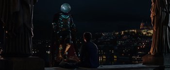 Movie still from “Spider-Man: Far from Home” (2019), directed by Jon Watts – A man sitting next to a statue at night; Medium shot, Over the shoulder angle