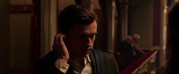 Movie still from “Spider-Man: Far from Home” (2019), directed by Jon Watts – A man in a suit and tie holding his hand to his ear; Close Up shot, Over the shoulder angle