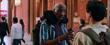 Movie still from “Spider-Man: Far from Home” (2019), directed by Jon Watts – A bald man with a neck brace holding a cup of coffee; Medium shot, Over the shoulder angle