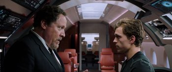 Movie still from “Spider-Man: Far from Home” (2019), directed by Jon Watts – Two men in suits are talking in a train car; Medium shot, Over the shoulder angle