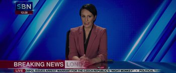 Movie still from “Spider-Man: No Way Home” (2021), directed by Jon Watts – A news anchor sitting at a desk in front of a microphone; Medium shot, Low angle