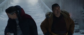 Movie still from “Spider-Man: No Way Home” (2021), directed by Jon Watts – A man in a brown jacket standing in front of a staircase; Medium shot, Over the shoulder angle