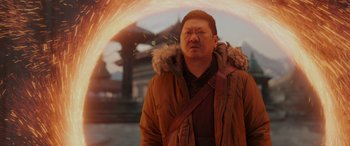 Movie still from “Spider-Man: No Way Home” (2021), directed by Jon Watts – A man in a brown jacket standing in front of a fire; Medium shot, Over the shoulder angle