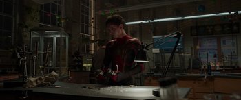 Movie still from “Spider-Man: No Way Home” (2021), directed by Jon Watts – A man in a red and black suit working in a workshop; Medium shot, Over the shoulder angle