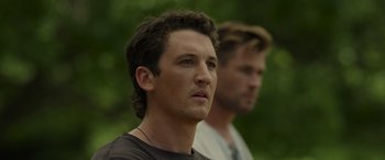 Movie still from “Spiderhead” (2022), directed by Joseph Kosinski – A man standing next to another man in a forest; Close Up shot, Over the shoulder angle